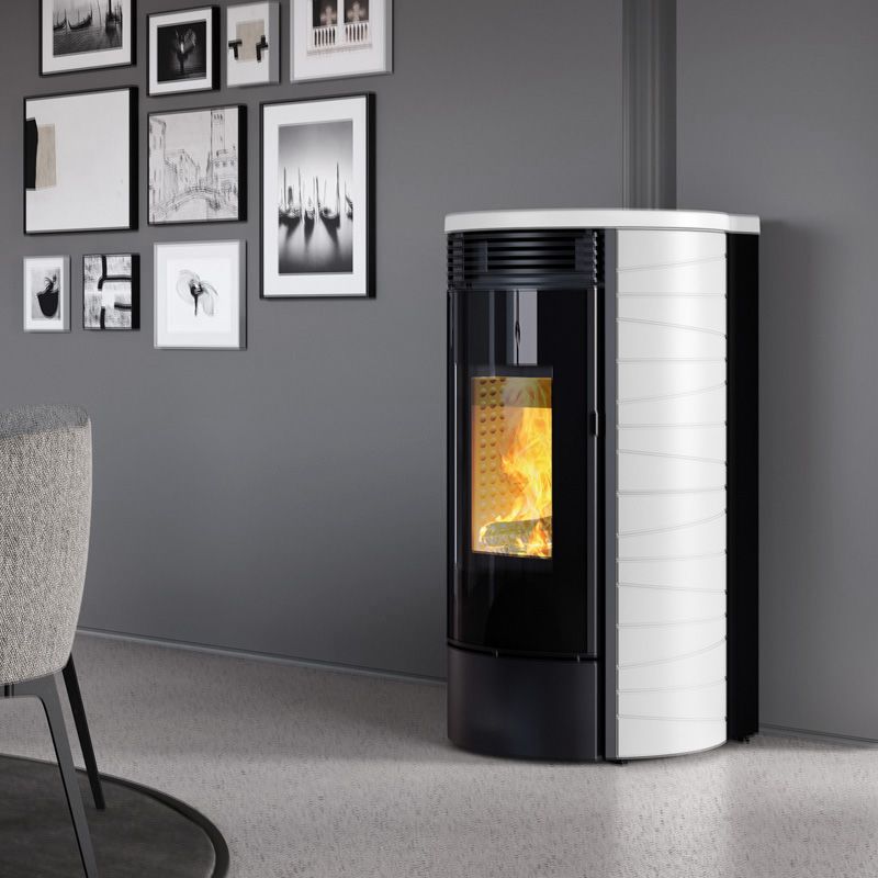 Termostufa a pellet Caminetti Montegrappa MW18 E GASSA M da 17,2 kW, con rivestimento in maiolica bianca e ampia fiamma a vista, ambientata in un soggiorno moderno dai toni neutri.
